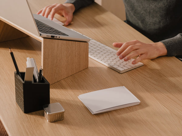 Person using a laptop and keyboard at a wooden desk with office supplies.  | light oak,