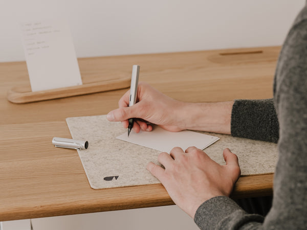 Person writing a to-do list with a pen at a wooden desk | oak