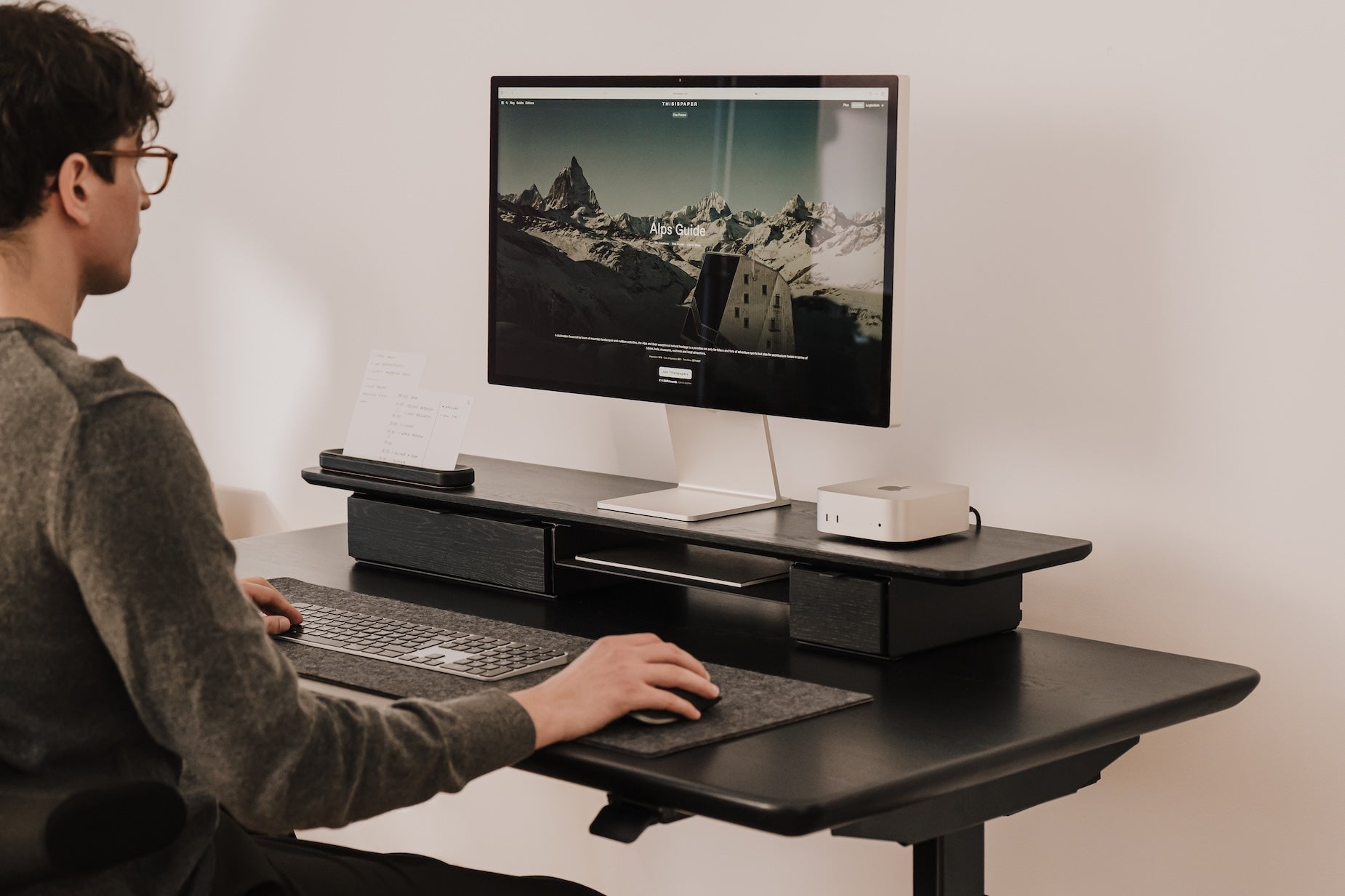 Person using a computer on a standing desk with a monitor displaying a snowy landscape | black