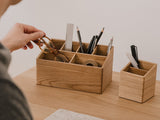 Person organizing stationery items in wooden desk organizers on a desk. | oak