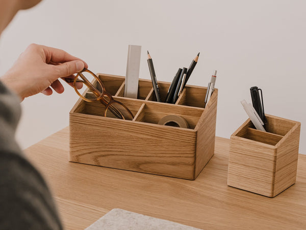 Person organizing stationery items in wooden desk organizers on a desk. | oak